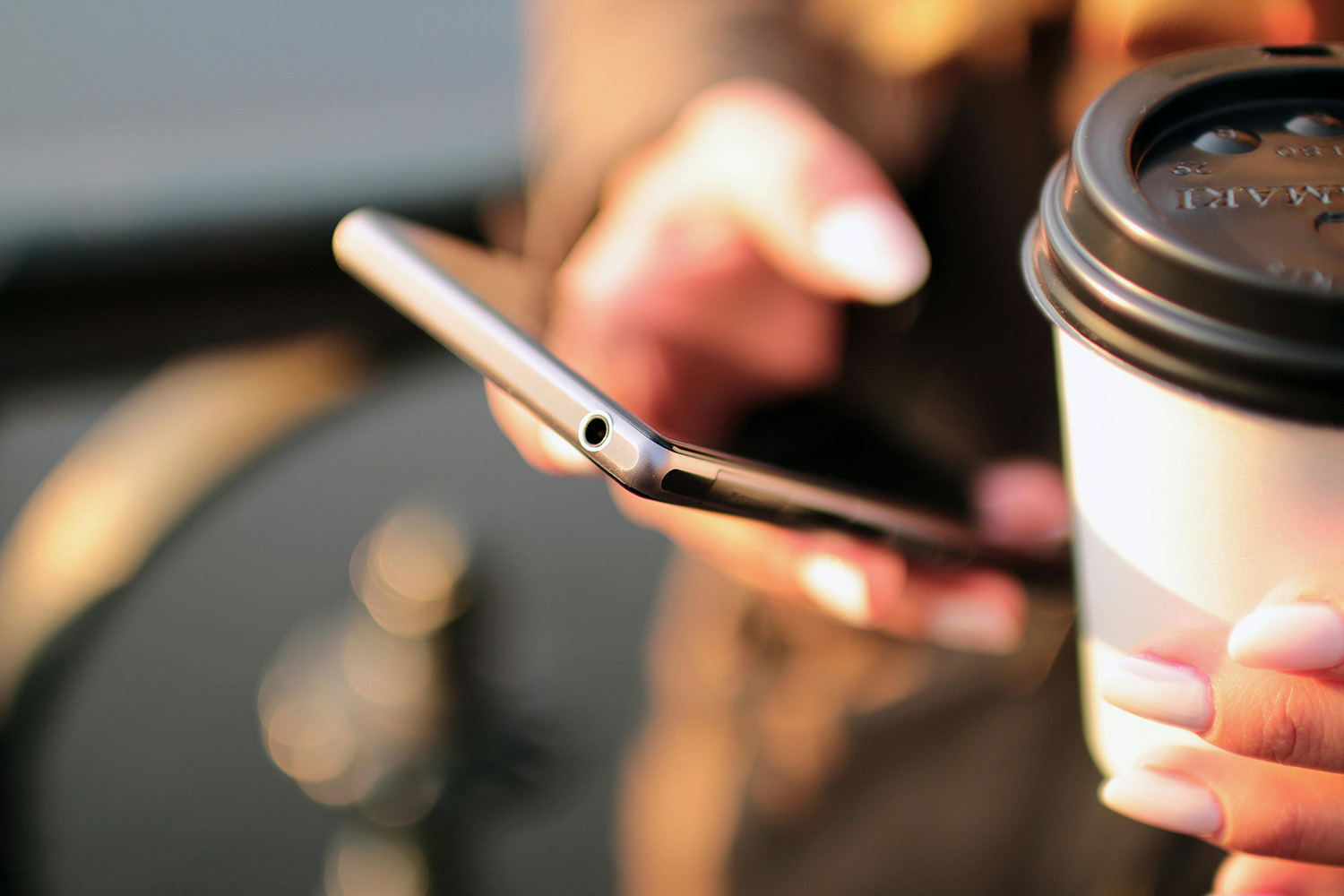 Close up of someone with a mobile phone and cup of coffee